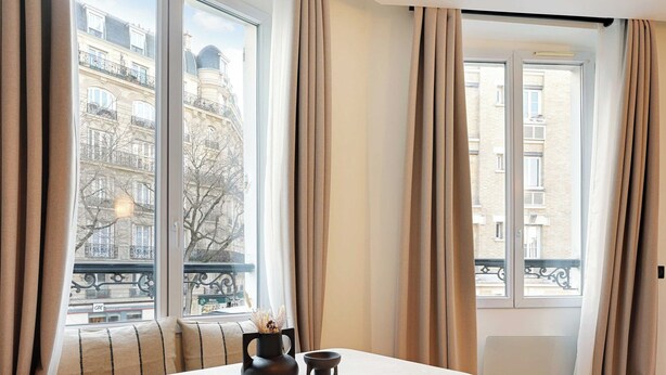 A modern dining area with a wooden table and chairs, large windows with curtains, and a view of the cityscape. - Elegant Apartment - 1br/4p - Sacre-coeur (Paris)