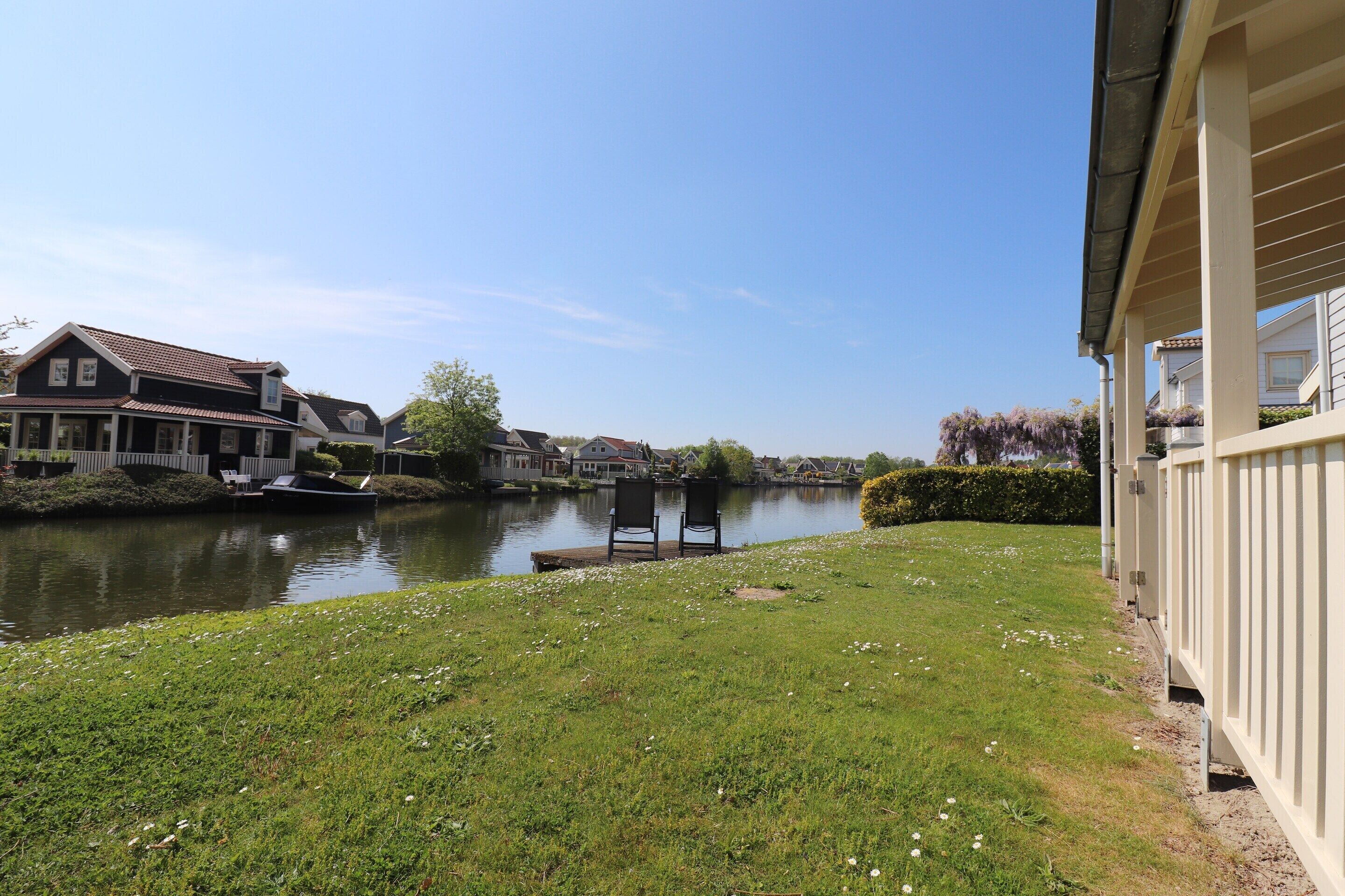 A riverside view with a grassy area, a chair, and a building with a balcony.