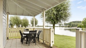 A covered patio with a table and chairs, overlooking a lake and surrounded by trees. - Bungalow by Water Near Rotterdam With Sauna (Simonshaven)