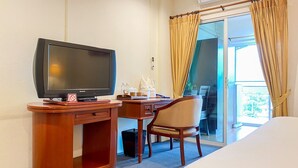 Habitación de hotel con un escritorio de madera, televisor, silla, cama y vistas al exterior a través de un ventanal.