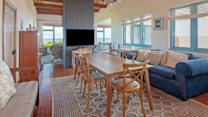 A spacious living room with a wooden dining table, blue sofa, and a large TV.