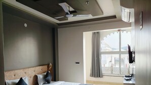 Habitación de hotel con cama, ventilador de techo, ventana con cortinas y televisor montado en la pared.