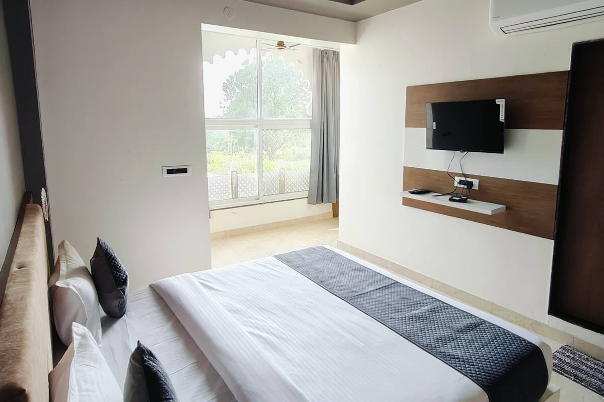 Habitación de hotel moderna con una cama grande, televisor de pantalla plana, ventilador de techo y un amplio ventanal con vistas a la vegetación.