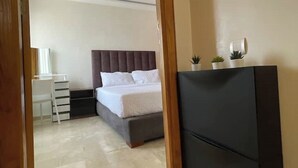 Quarto com cama, mesa de cabeceira e escrivaninha com gavetas.