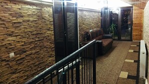 A hallway with a stone wall, a black door, a brown sofa, and a small table with a plant. - The Sindh House Tbilisi (Tbilisi)
