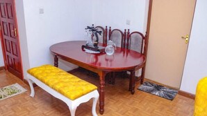 Ein Essbereich mit einem Holztisch, vier Stühlen, einer Bank mit gelber Sitzkissen und einer Tür im Hintergrund.