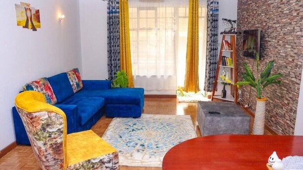 Ein Wohnzimmer mit einem blauen Sofa, einem gemusterten Sessel, einem runden Holztisch und einem Bücherregal.