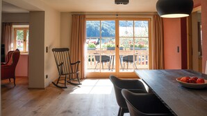 Un comedor con una mesa de madera, sillas negras, una mecedora y vistas a un jardín a través de un ventanal.
