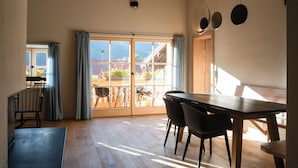 A spacious room with a wooden dining table, black chairs, and a view through large sliding glass doors to an outdoor area with potted plants. - 03 Michl, 85 sqm, 2 bedrooms, balcony, sauna, tiled stove (Schleching)