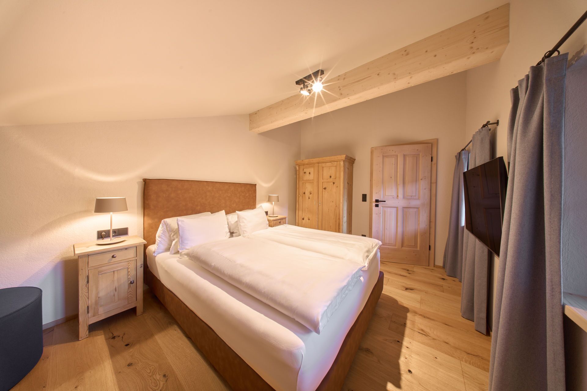 A bedroom with a large bed, wooden wardrobe, and a nightstand with a lamp.