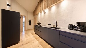 A modern kitchen with a wooden ceiling, a black refrigerator, a sink, and a coffee maker. - 03 Michl, 85 sqm, 2 bedrooms, balcony, sauna, tiled stove (Schleching)