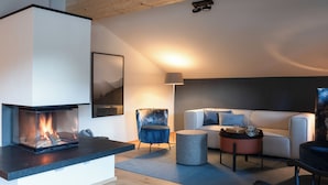 A modern living room with a fireplace, a sofa, a chair, and a coffee table. - 03 Michl, 85 sqm, 2 bedrooms, balcony, sauna, tiled stove (Schleching)