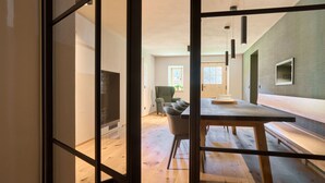 A modern interior with a wooden dining table, a green armchair, and a television in a corner.