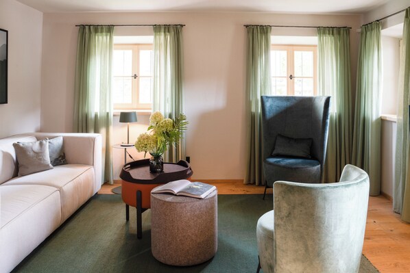 A living room with a sofa, ottoman, round table with a vase, and a chair.