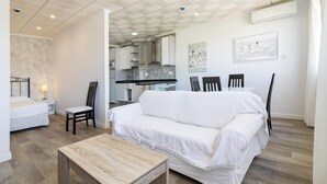 A modern living room with a white sofa, a wooden coffee table, and a dining area with chairs.
