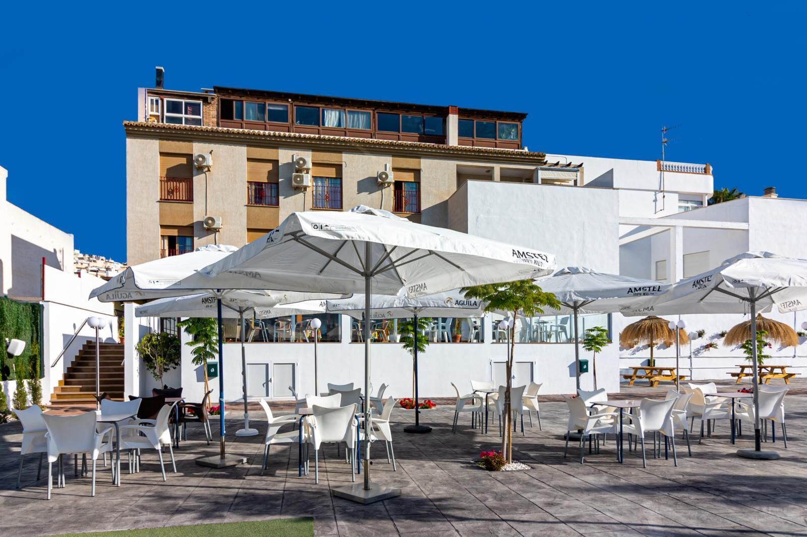 An outdoor seating area with white chairs and umbrellas, a staircase, and a building with balconies in the background.
