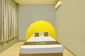 A hotel room with a bed, curtains, and a wall-mounted air conditioner.