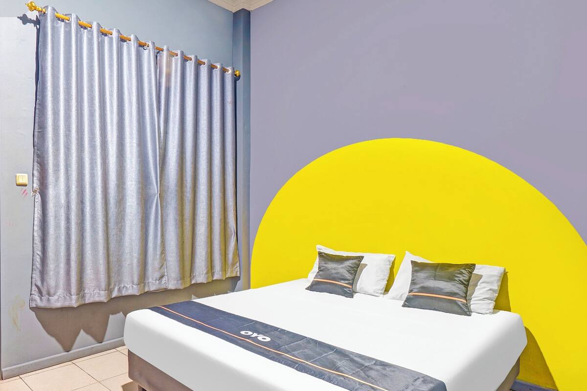 A bed with a white mattress and a blue headboard, a grey curtain, and a yellow wall.