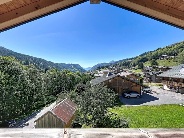 Une vue depuis un balcon en bois donnant sur un village avec ses maisons traditionnelles, une route et un paysage montagneux en arrière-plan.