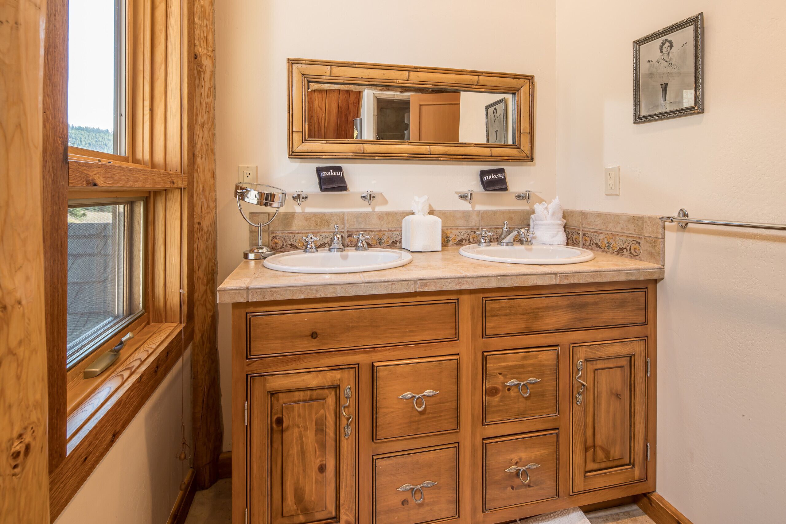 Une coiffeuse en bois avec deux vasques, un miroir et une fenêtre.