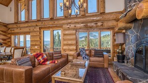 A log cabin interior with leather sofas, a glass coffee table, and a stone fireplace.