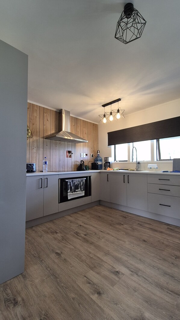 A modern kitchen with wooden cabinets, a built-in oven, and a black countertop. - Set Sail for Relaxation.
Cosy Beachside Cottage at Port Charles. (Port Charles)