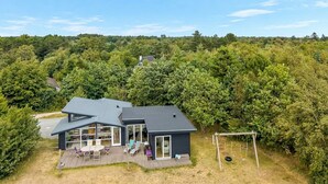 Ein modernes Haus mit einer Terrasse und einer Schaukel, umgeben von dichtem Wald.