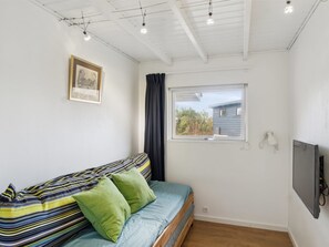 A small, well-lit room with a single bed, a window with a view of a house, and a mounted television.