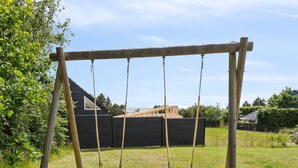 Eine Holzschaukel im grünen Garten mit einem schwarzen Zaun und einem Haus im Hintergrund.