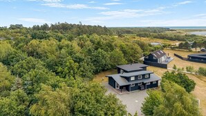 Ein Wohngebiet mit modernen Häusern, umgeben von dichtem Wald, strahlend blauem Himmel und weiter Sicht auf das Meer.