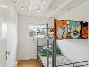 A bunk bed room with a window, a radiator, and a wall-mounted coat rack with bags.