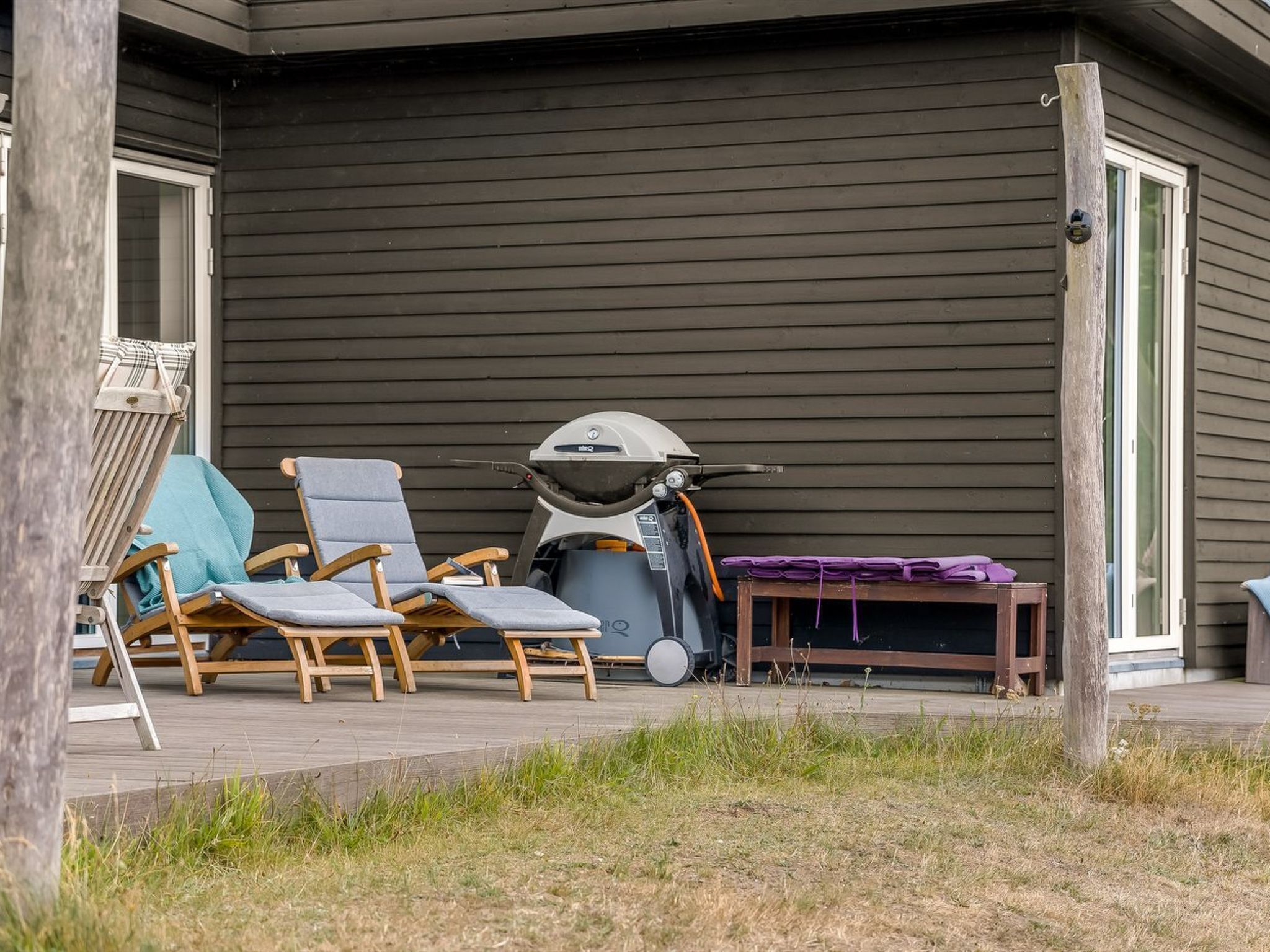 A covered outdoor seating area with lounge chairs and a barbecue grill.