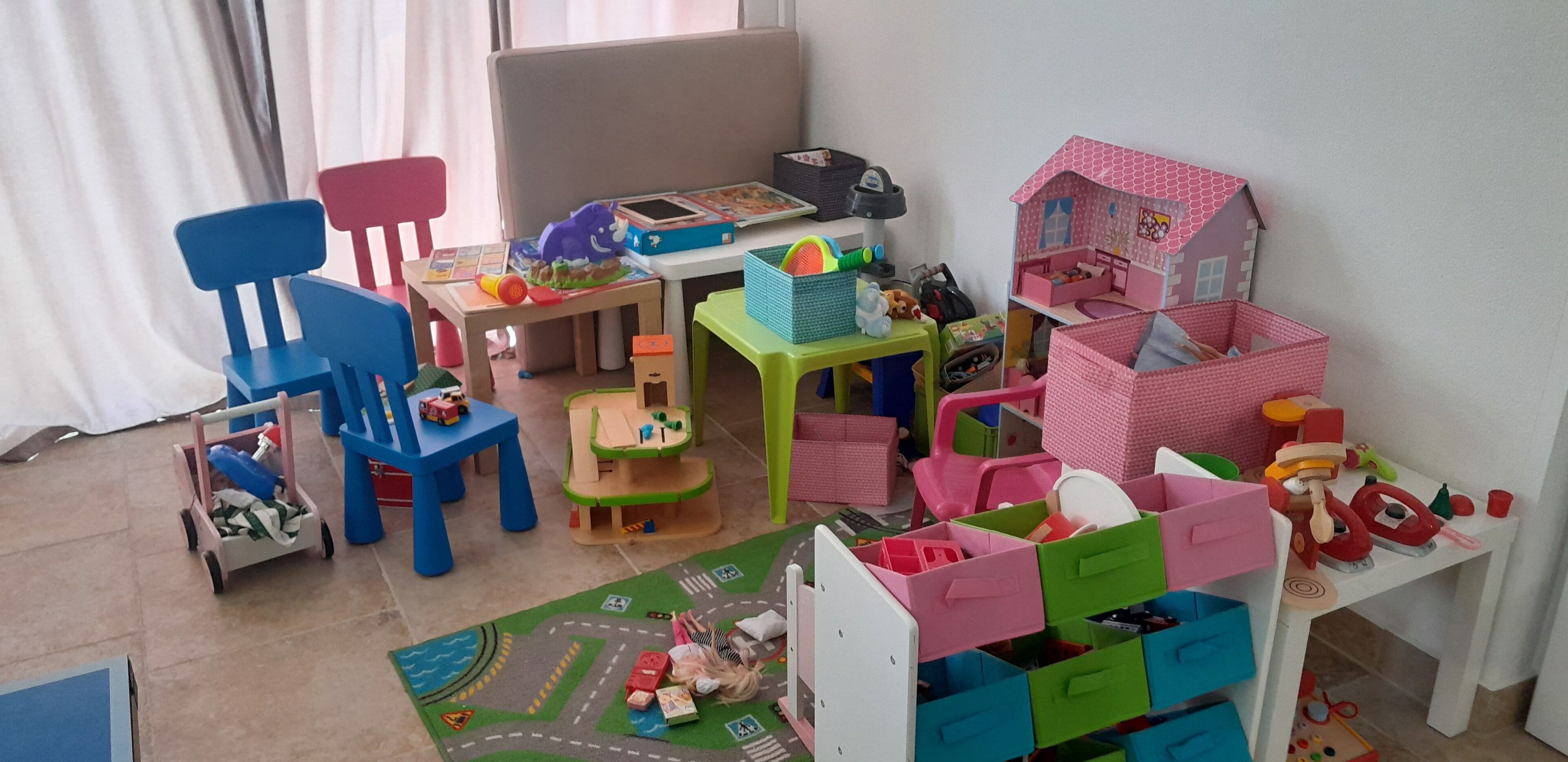 A child's playroom with a wooden table, chairs, a play mat, and various toys.