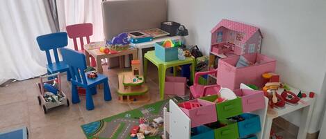 A child's playroom with a wooden table, chairs, a play mat, and various toys.