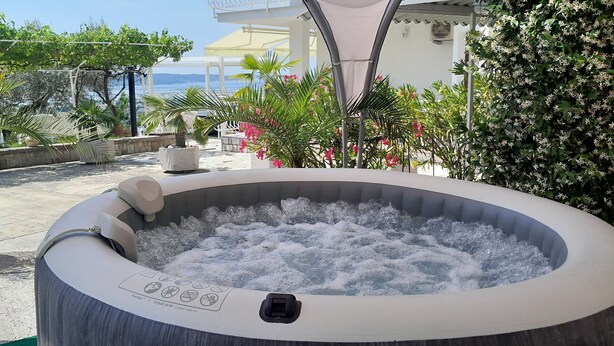 An outdoor hot tub with a view of the sea, surrounded by potted plants and outdoor furniture. - Apartments Milok (Piran)