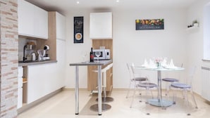 A modern kitchen with white cabinets, a wooden accent wall, a coffee machine, a wine bottle, and a glass on the counter. - Apartments Milok (Piran)
