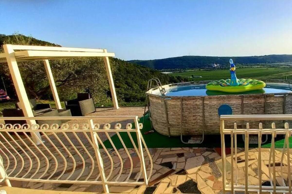A hot tub with a view of a hilly landscape, a pergola, and a fenced patio area.