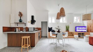 A modern kitchen with a wooden countertop, a bar stool, and a dining area with a round table and chairs.