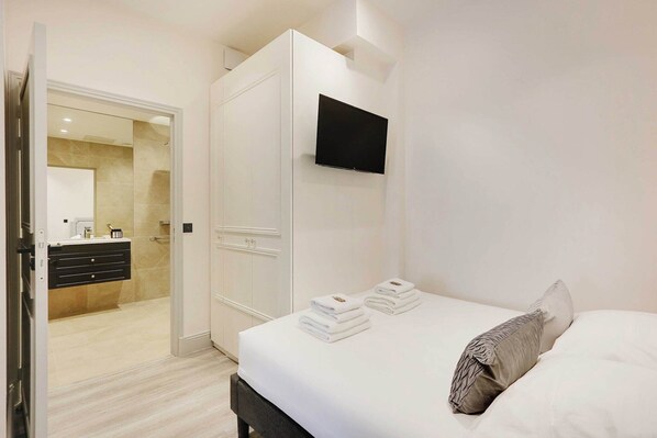 Une chambre d’hôtel avec un lit, un téléviseur fixé au mur et une salle de bain visible à travers une porte ouverte.