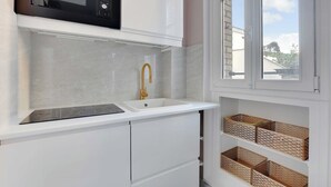 A kitchen with a white countertop, a gold faucet, a microwave, and wicker baskets on shelves.