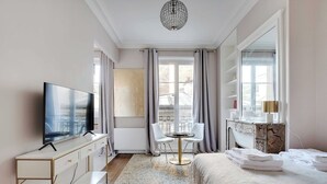 A hotel room with a TV, a desk, a chair, a bed, and a window with curtains.