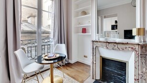 A modern living room with a fireplace, a dining area with two chairs and a table, and a large window with curtains.