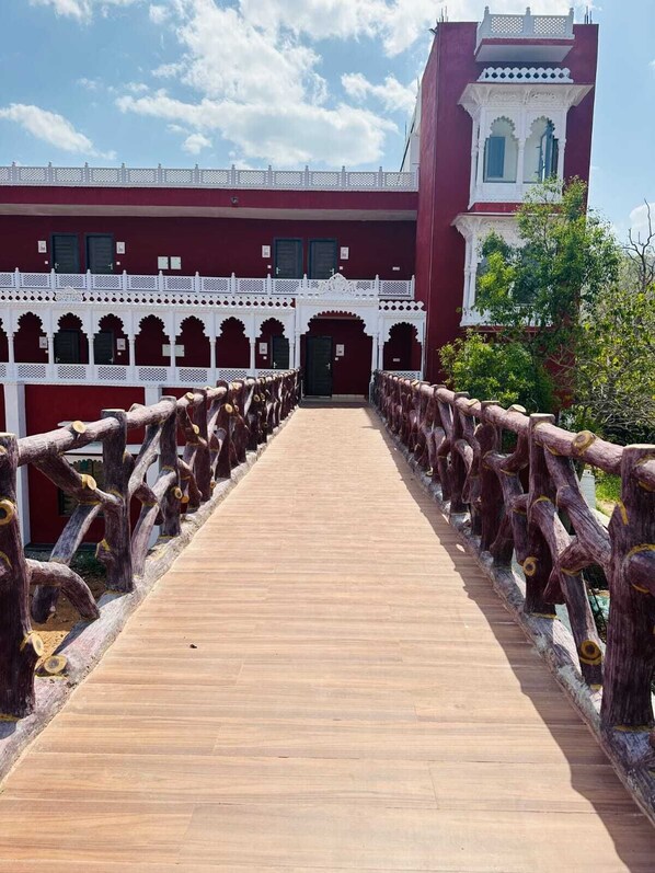 A wooden bridge leading to a building with arched doorways and a red facade.