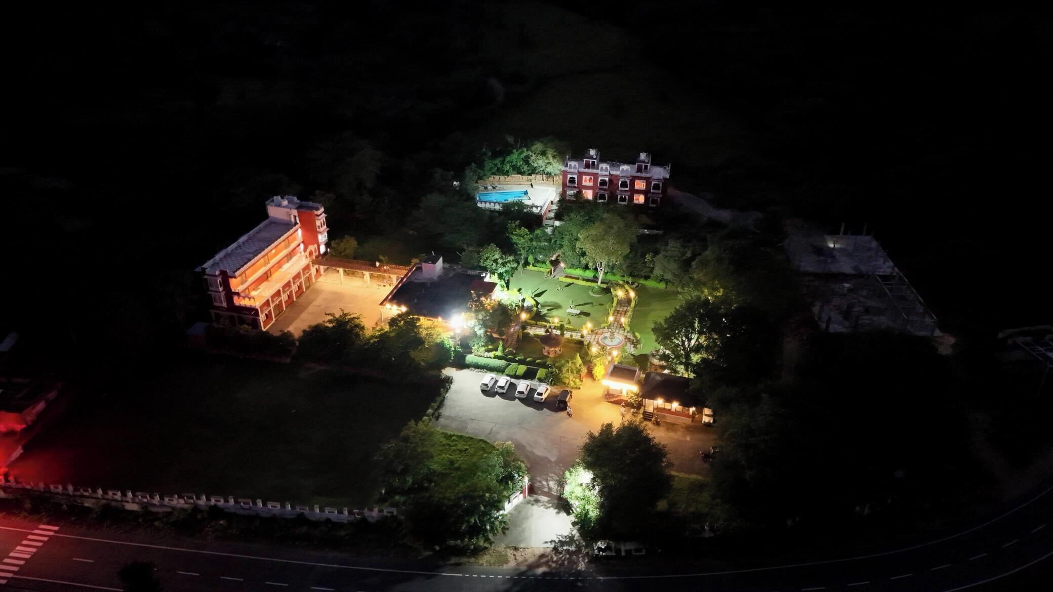 An aerial view of a well-lit area with a large building, a swimming pool, and a parking lot.