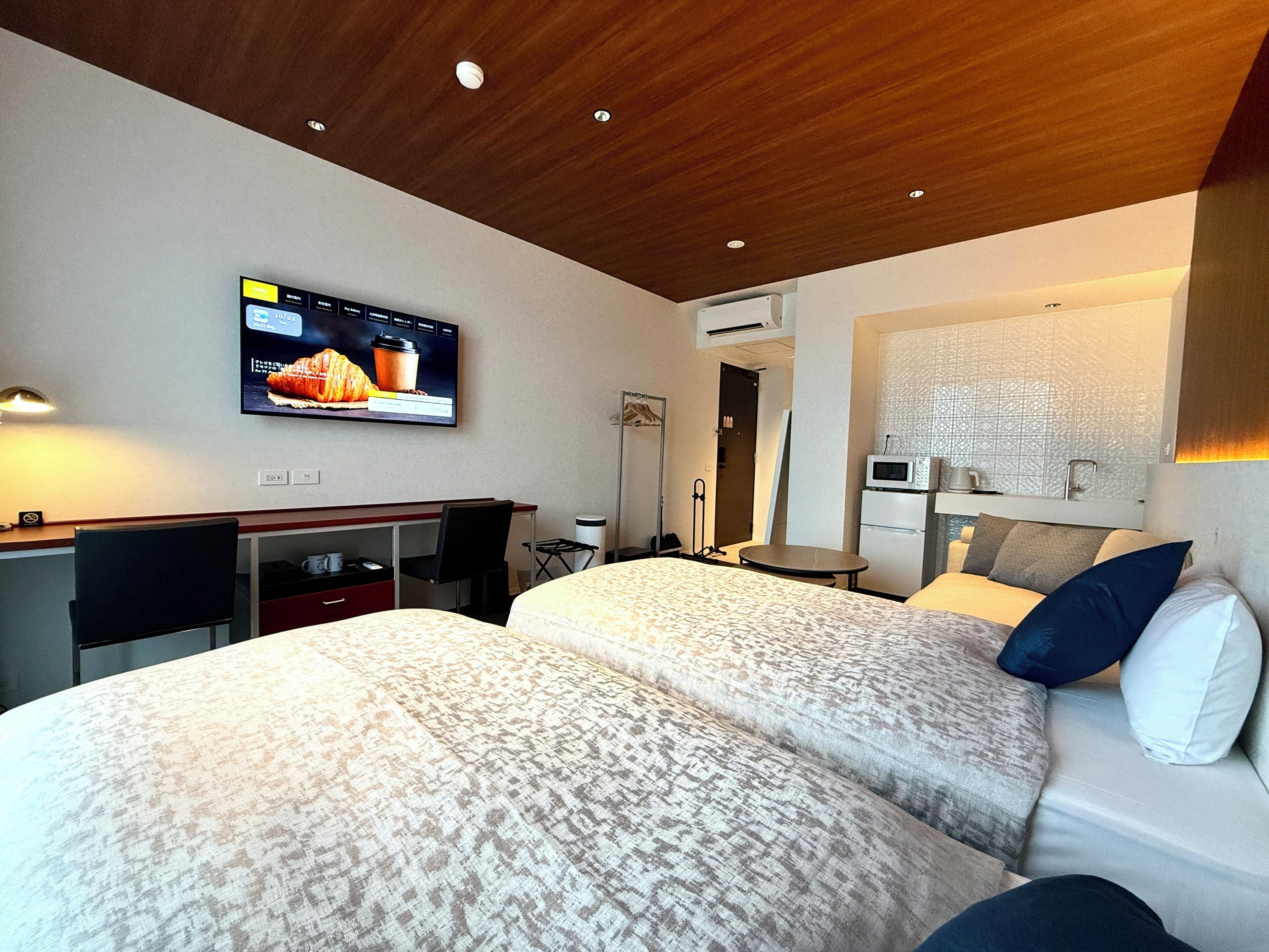 A hotel room with two beds, a desk, a TV, a microwave, and a small table.