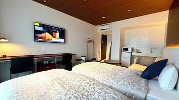 A hotel room with two beds, a desk, a TV, a microwave, and a small table.