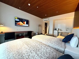 Habitación de hotel con dos camas, un escritorio, televisor, microondas y una mesita.