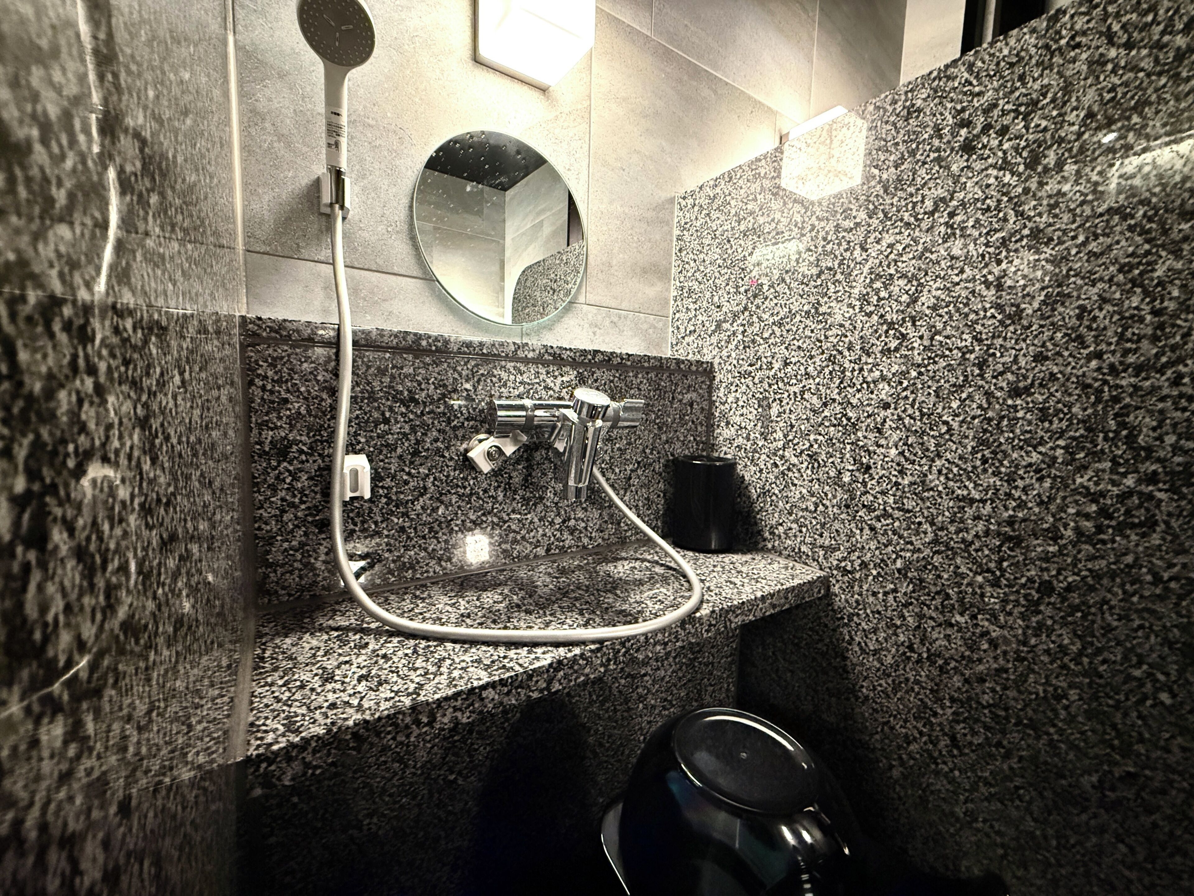 A modern bathroom with a granite countertop, a handheld showerhead, a sink, and a mirror.