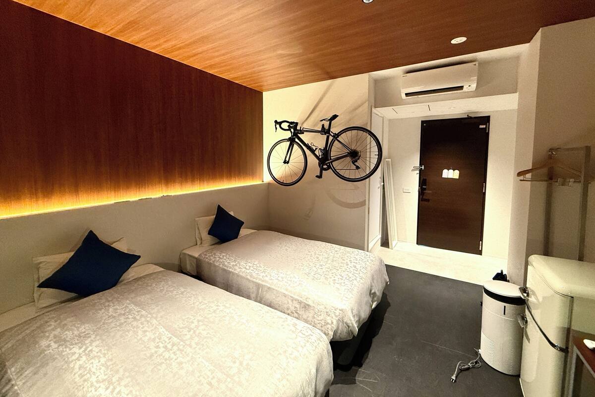 Ein modernes Hotelzimmer mit zwei Betten, einem an der Wand befestigten Fahrrad und einer Tür zu einem Badezimmer.