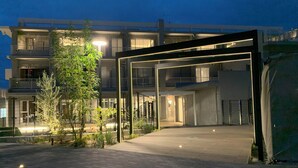 Un bâtiment moderne doté d’une entrée couverte, de nombreux balcons et d’un espace extérieur bien éclairé, avec un revêtement de sol pavé.